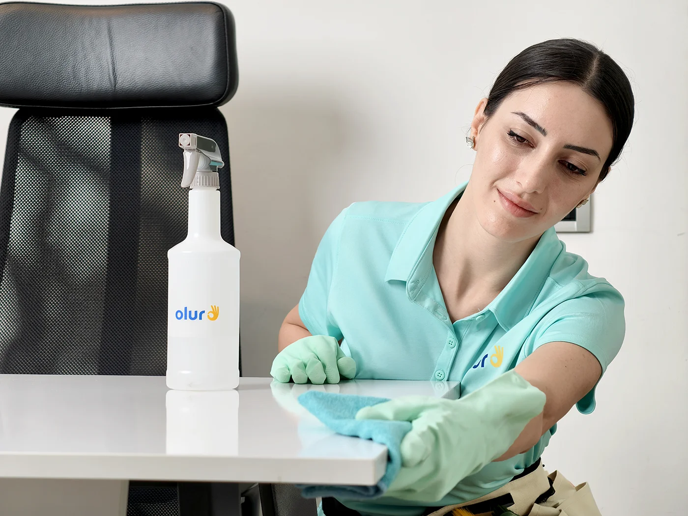 Olur ofis temizlik görevlisi, sprey temizleyici şişesi ve mikrofiber bezle ofis masasını siliyor